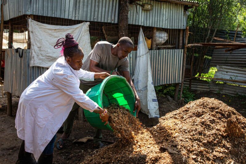 A woman in a lab coat transforming agriculture for young people by pouring dirt into a bucket.