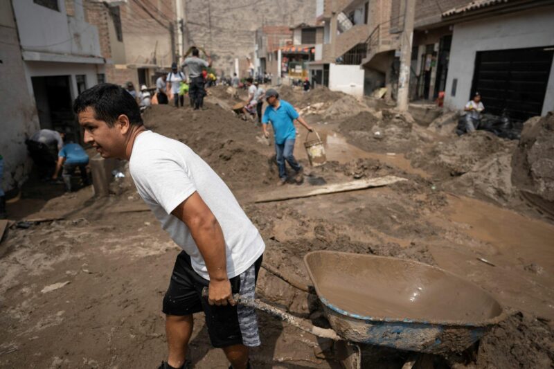 A man navigates a flooded street with a wheelbarrow. Cyclone Yaku aftermath in Peru