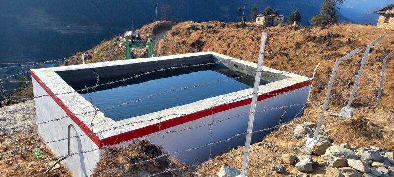 A water tank on top of a hill with a fence around it, helping turn the tables on climate change in Nepal.