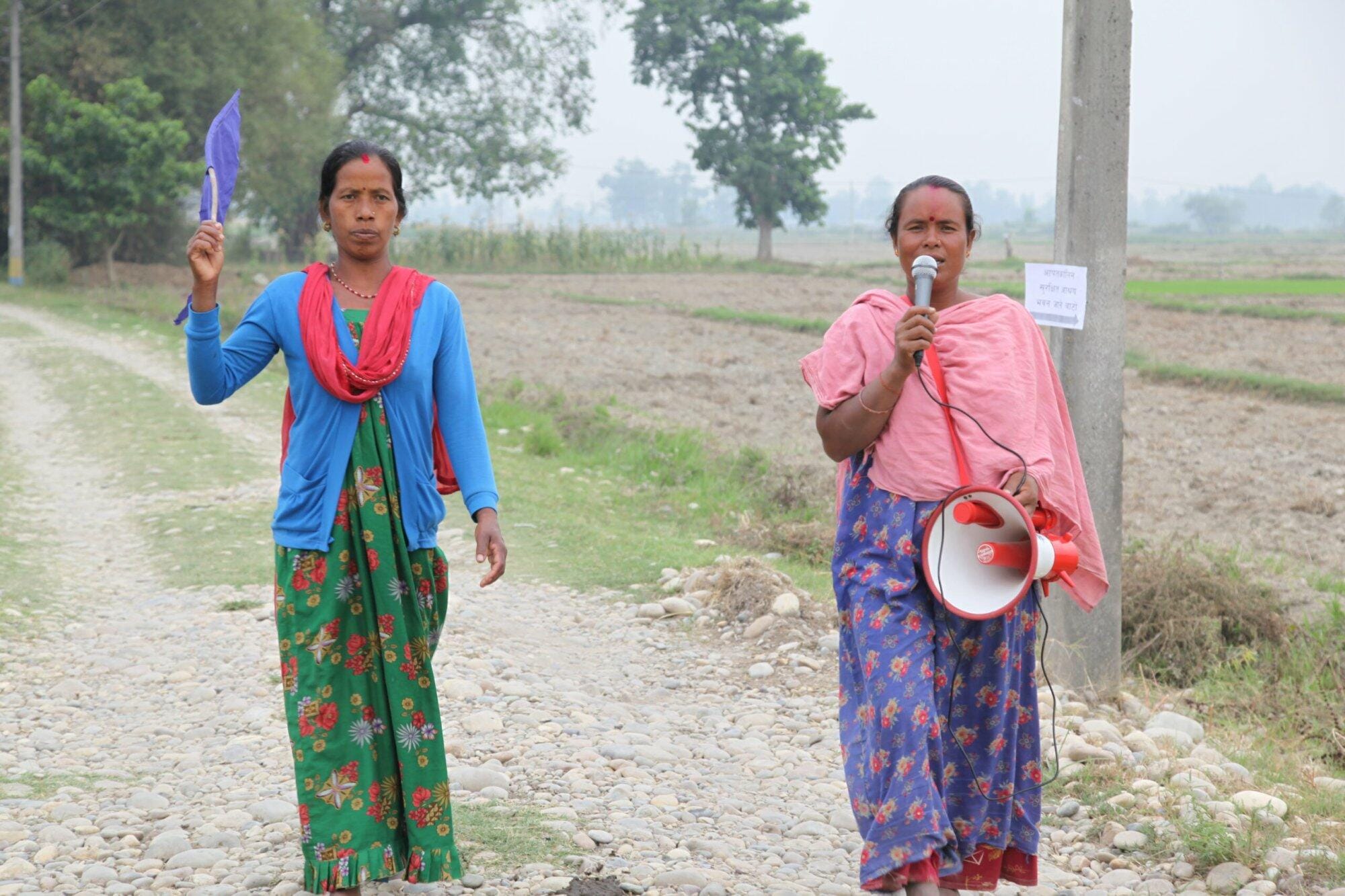 Two women implementing Practical Action in Nepal, standing on a dirt road with a megaphone.