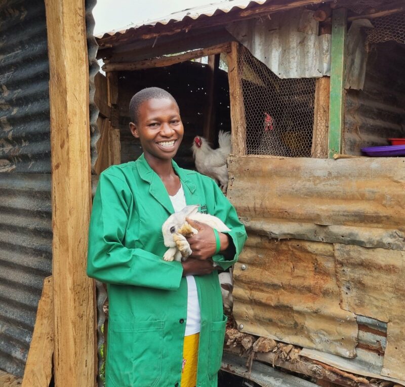 A woman holding a bunny in front of a shack, promoting Transforming Agriculture for Young People.