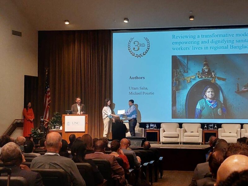A group of people standing in front of a large screen at the Sanitation Workers Research Awards.