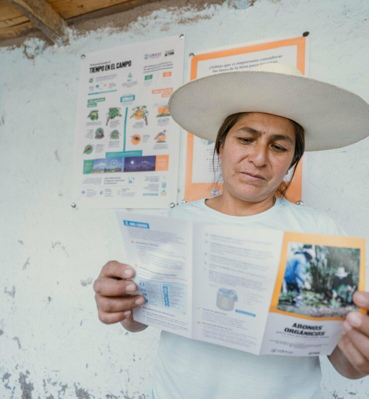 A woman in a hat is holding a brochure promoting resilient communities in Peru (BHA).