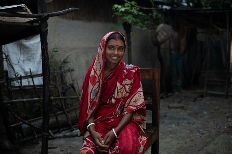A woman in a red sari sitting on a wooden chair, symbolizing growing hope in Bangladesh.