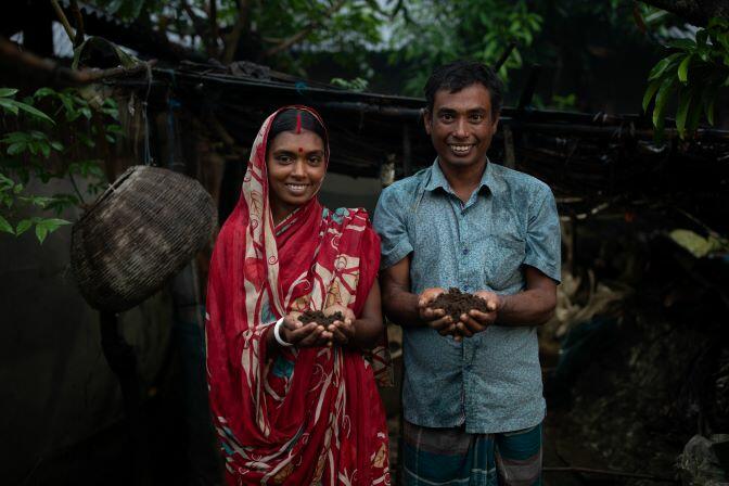A man and a woman in a sari standing next to a tree in Bangladesh, embodying growing hope as worms save lives.