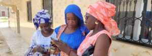 Three women in Senegal are empowering themselves by addressing climate challenges while looking at their cell phones.
