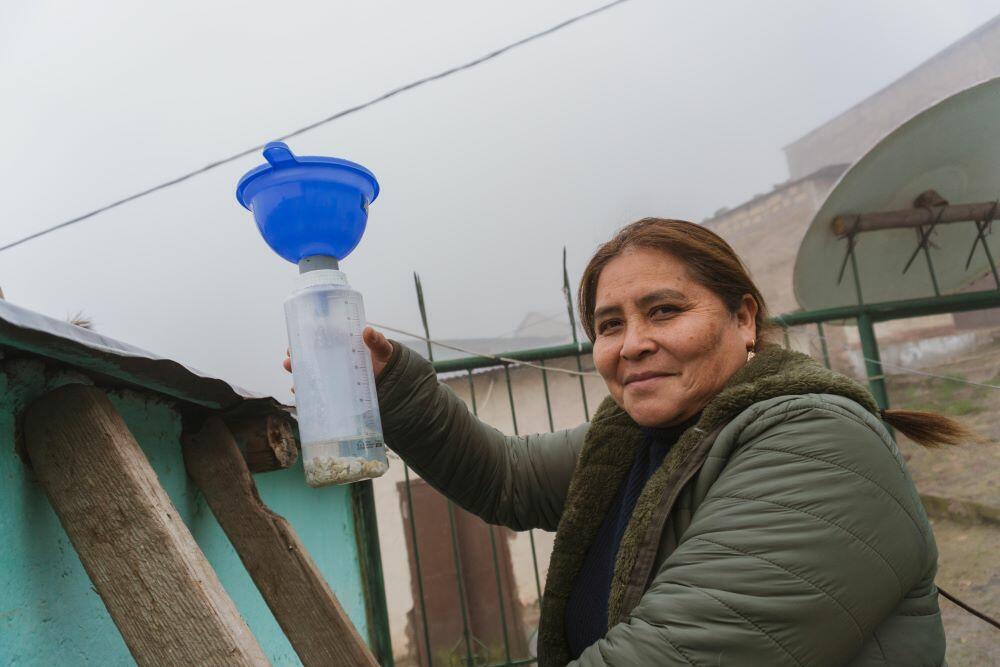 A woman from Practical Action en Peru holding a blue water bottle in front of a house.