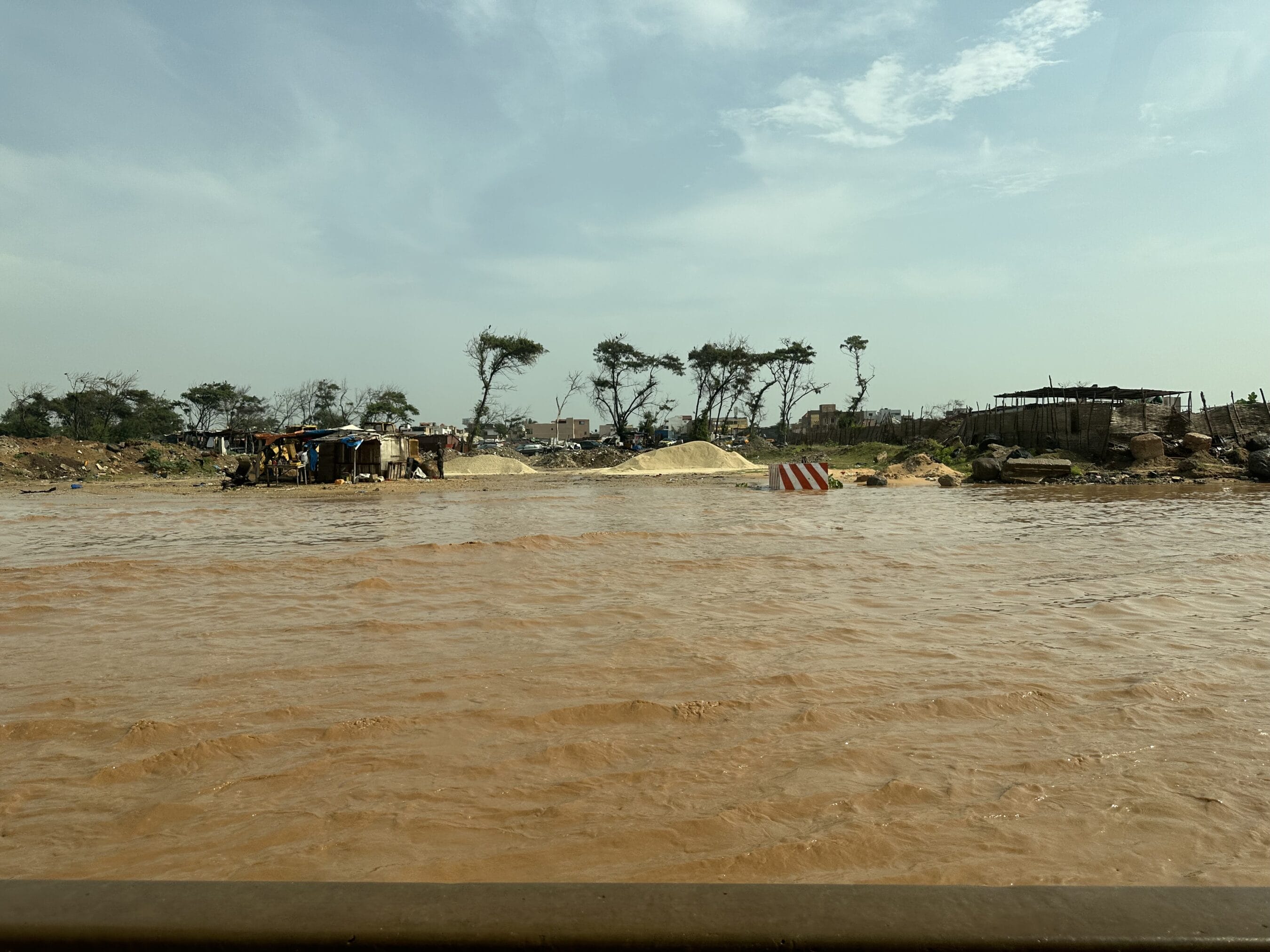 A view of a muddy river in West Africa with a few houses in the background.