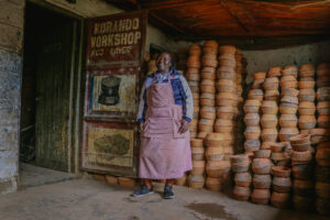 Lillian, a woman in an apron, standing in front of a pile of clay, inspiring and thriving.