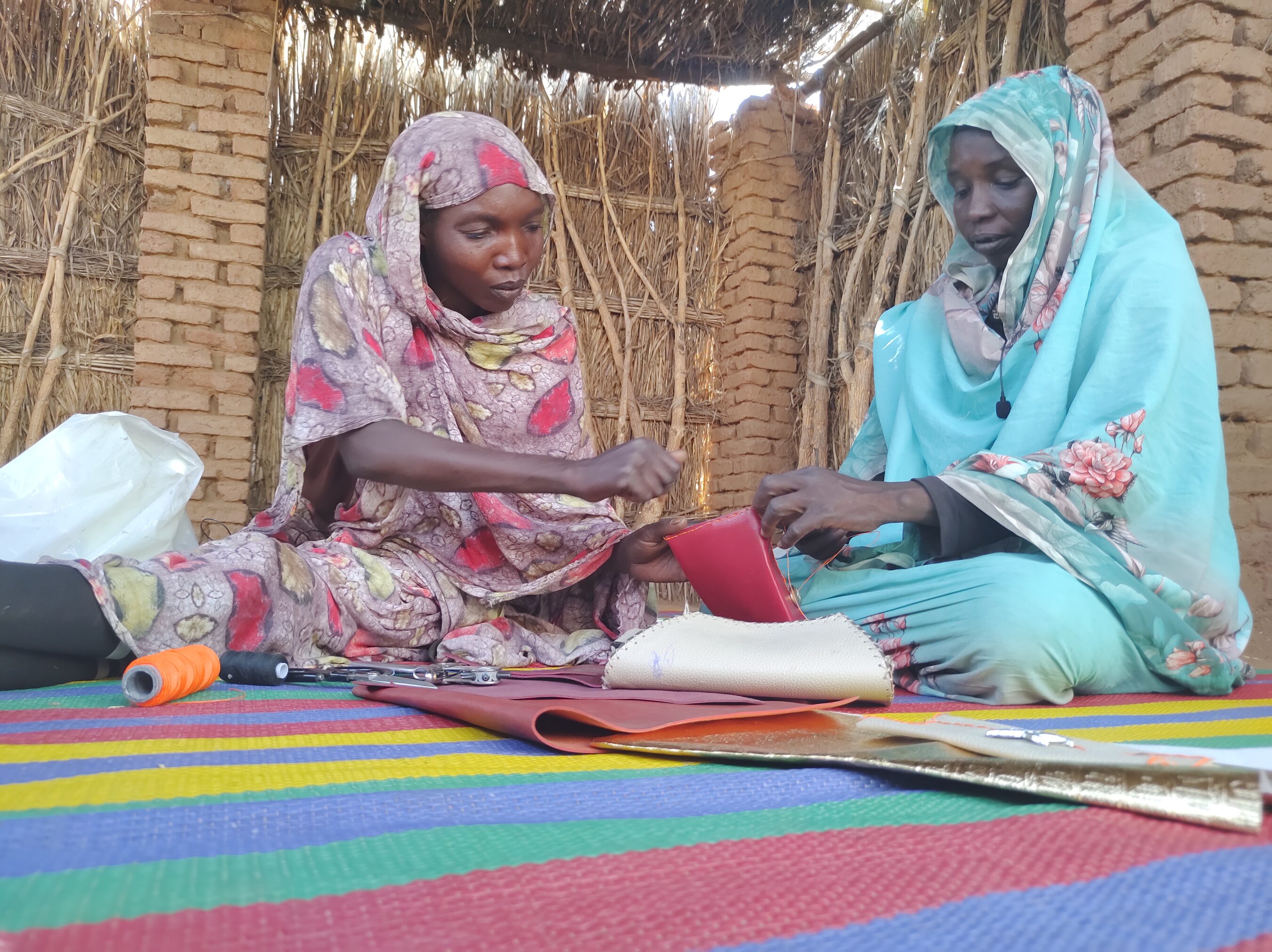 Two women in a hut determinedly working on a piece of cloth, finding empowerment amidst desolation.