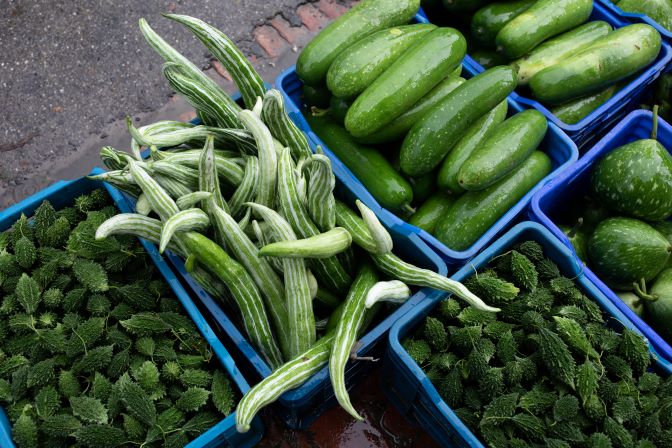 A selection of Bangladeshi farmers' cucumbers and green beans in blue crates on a sidewalk, showcasing hope amidst floods.