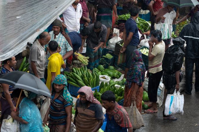Floods leave Bangladeshi farmers standing in a market with umbrellas, searching for hope.