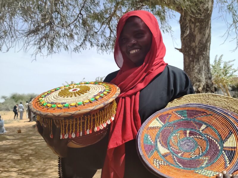 A woman wearing a red head scarf holding a colorful plate, emphasizing the Perspective of Gender-Based Violence in Practical Action Sudan.