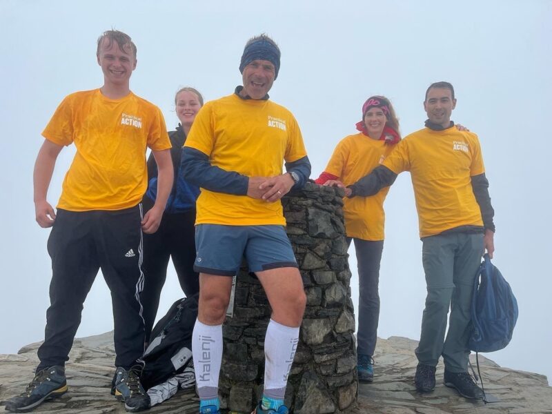 A group of people posing for a picture on top of a mountain, celebrating their fundraising success.