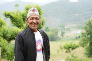 Hum Basnet in a hat smiling in front of a mountain.