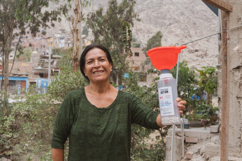 A woman holding a water bottle in front of a house, demonstrating resilience against potential floods.