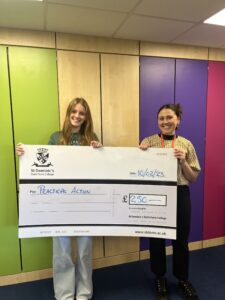 Two girls holding a fundraising check in front of a colorful room.