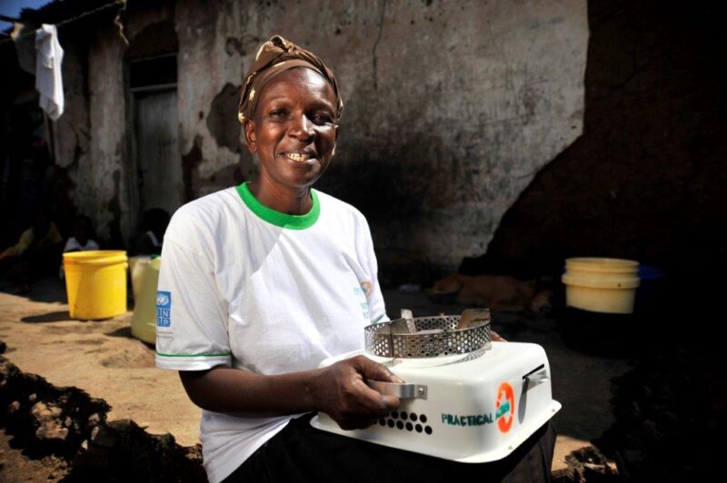 A woman in a white shirt holding a small stove, promoting a simple solution for Kenyan Lives.