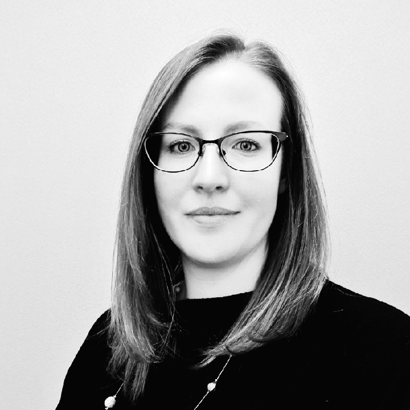 Black and white portrait of a woman with glasses smiling at the camera.