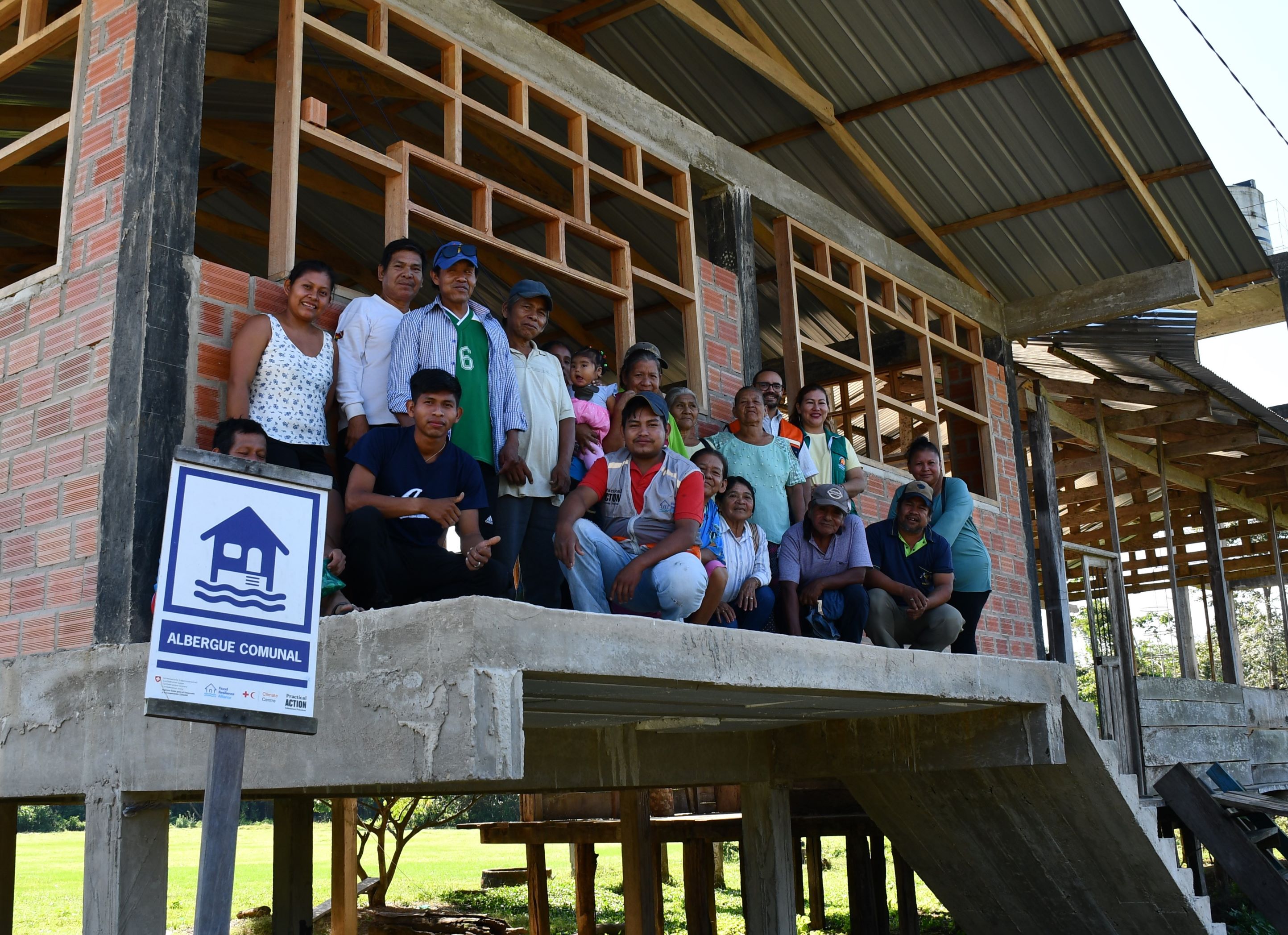 Group of people posing for a photo on the steps of a building under construction labeled "albergue comunal".
