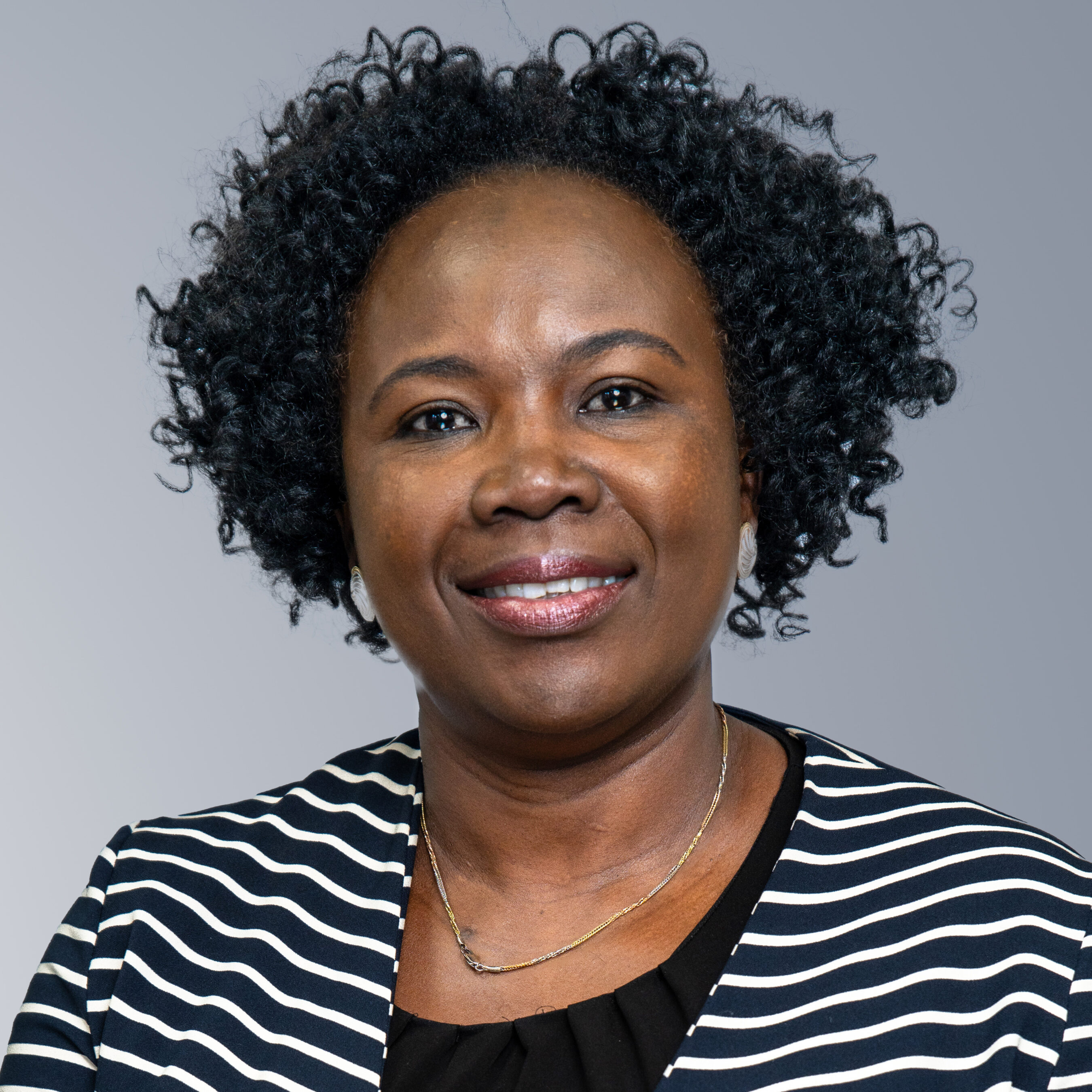 Akinyi Walender - A person with short curly hair wearing a black and white striped top smiles while facing the camera against a plain grey background.