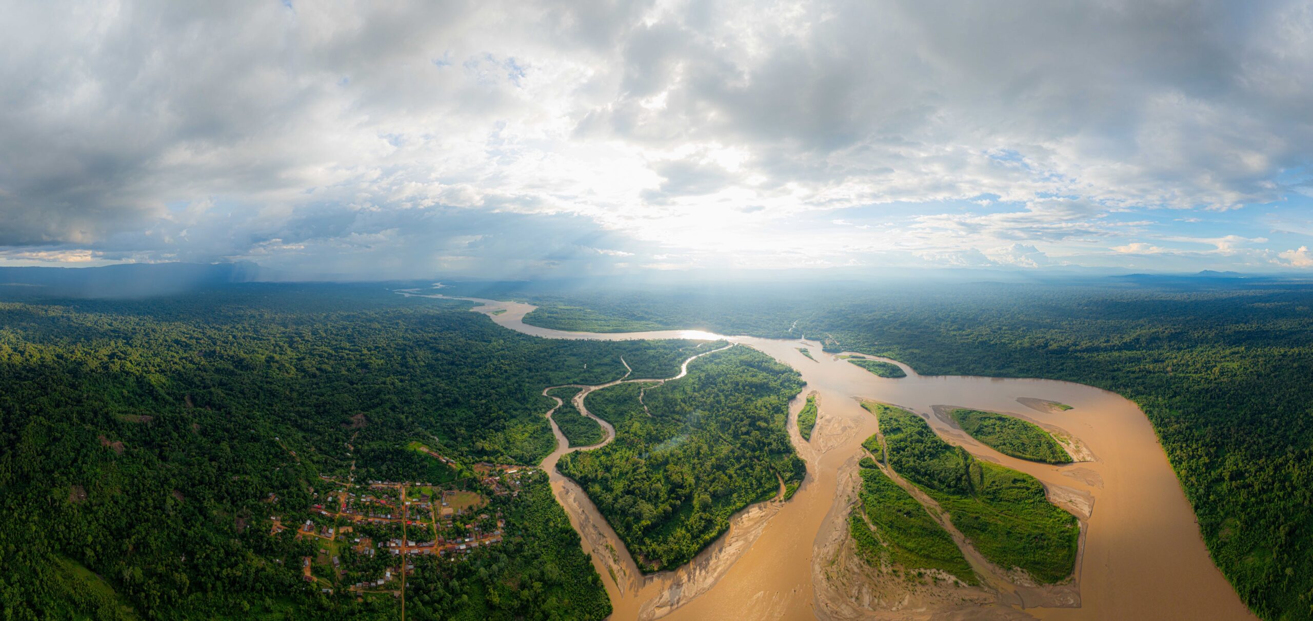 Aerial view of a winding river cutting through a lush, green forest landscape under a partly cloudy sky.