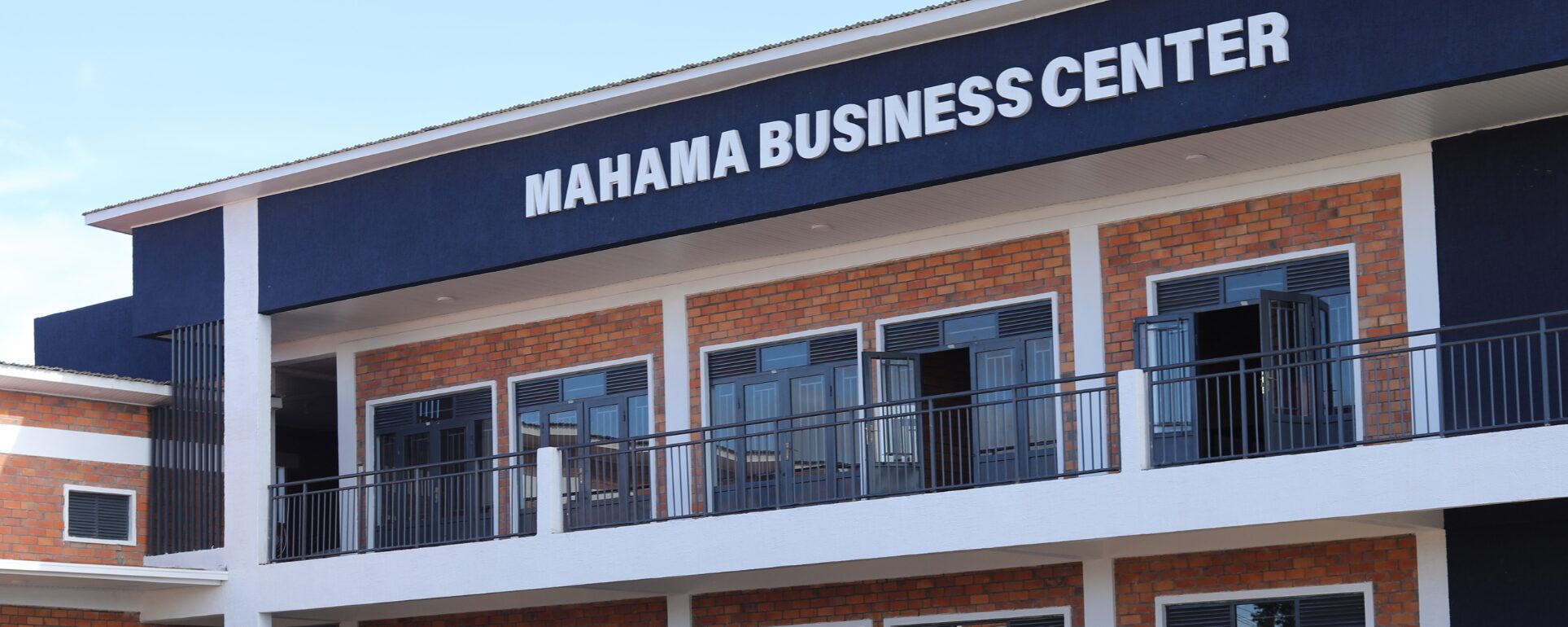 A two-story building with a sign reading "Mahama Business Center." It has brick walls, black railings, and several windows and doors.
