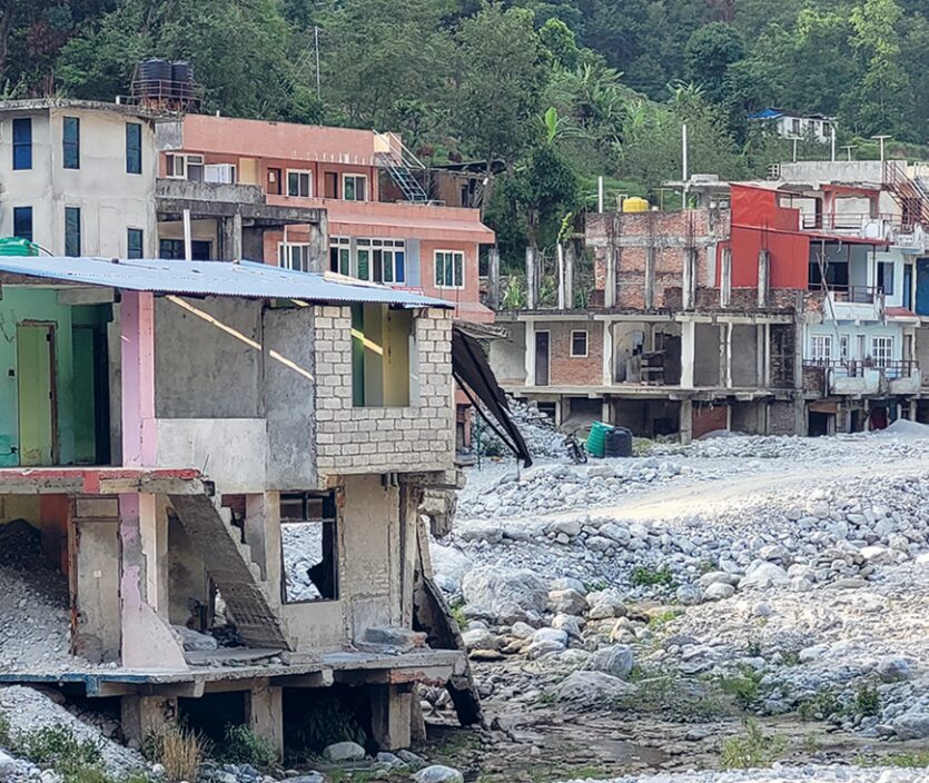Partially constructed and damaged buildings on rocky terrain, with greenery in the background.