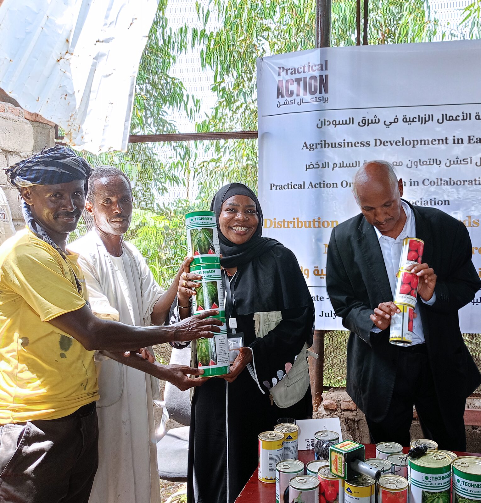 Four people stand together in front of a banner, holding and displaying cans of agricultural products at an agribusiness development event.