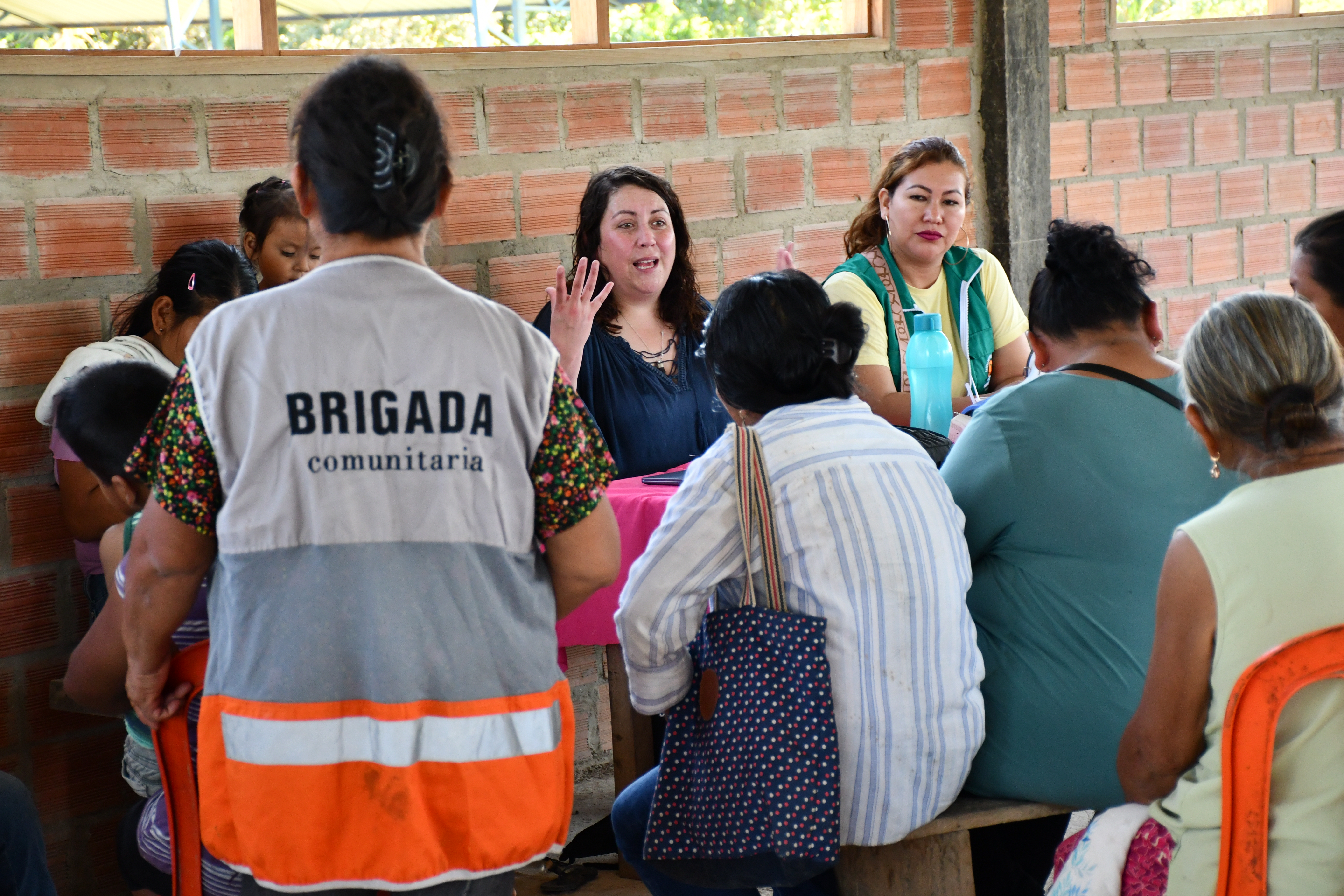 A group of women sit around a table in discussion, while a person in a 