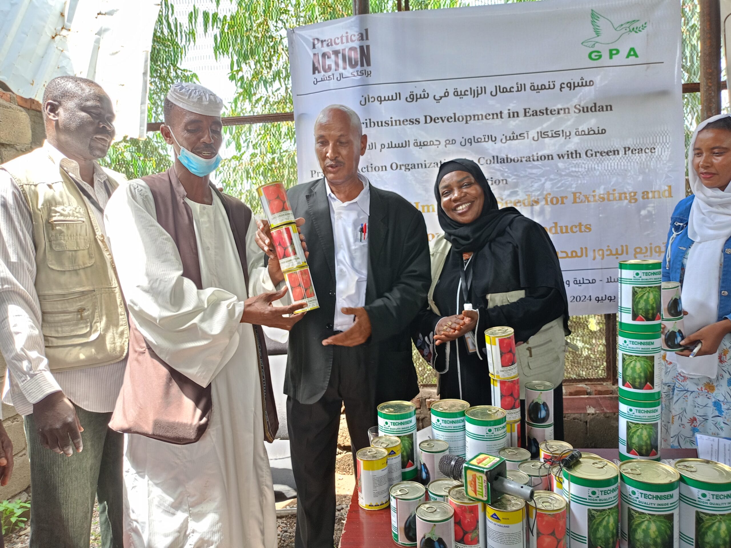 A group of people stand around a table displaying canned agricultural products in front of a banner about agribusiness development in Eastern Sudan.