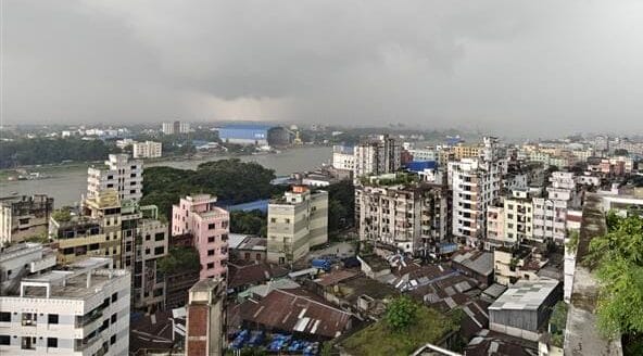 Panoramic view of a densely populated urban area with high-rise buildings under a cloudy, overcast sky; a river is visible in the background.