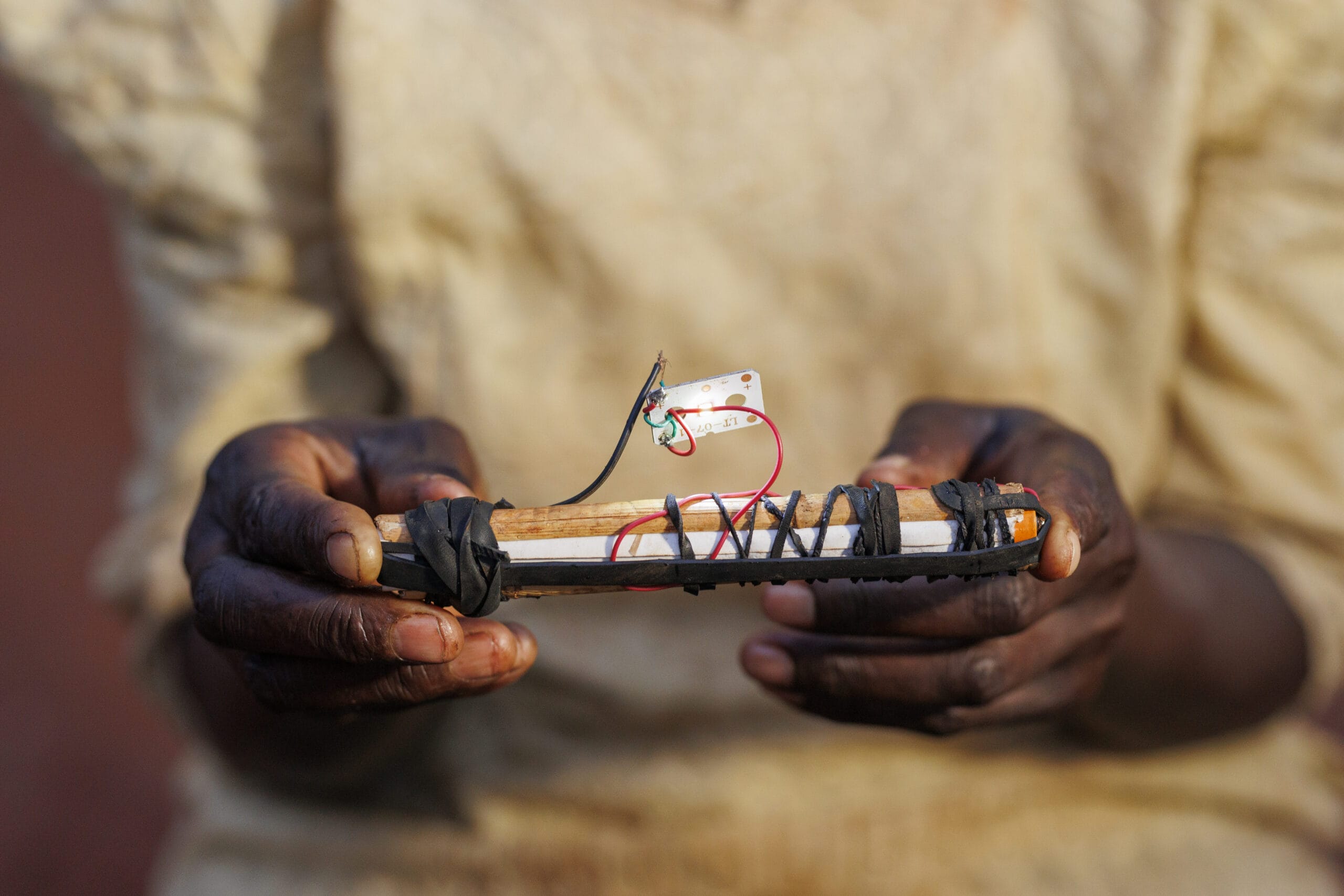 A person holding a homemade improvised device wrapped with wires and tape, constructed from various materials, with their hands clearly visible against a blurred background.