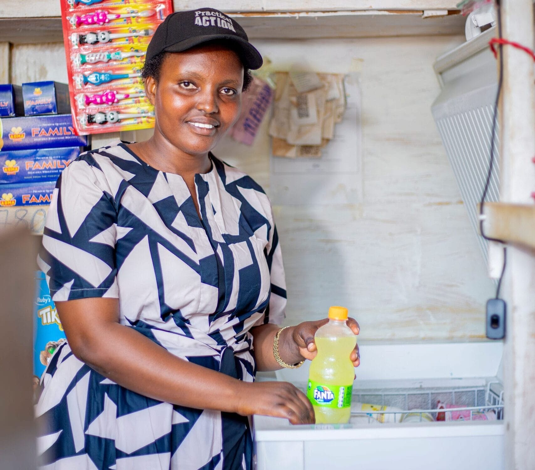Woman in a shop holding a Fanta bottle, surrounded by snacks and drinks, smiling at the camera.