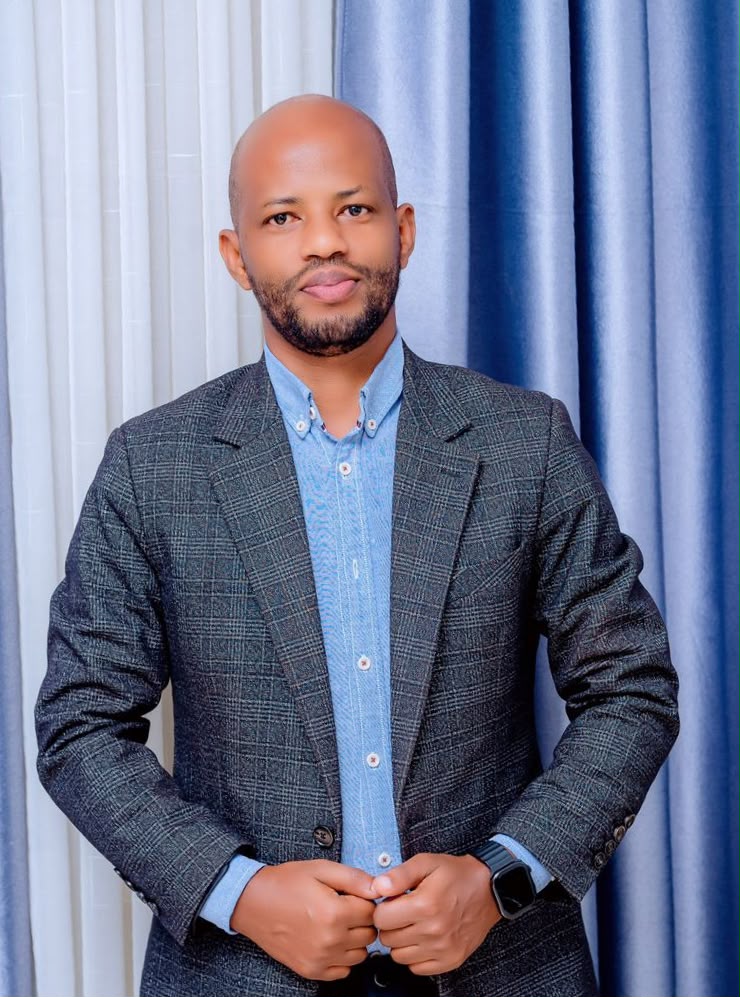 A man with a beard wearing a blue button-down shirt and a patterned jacket.